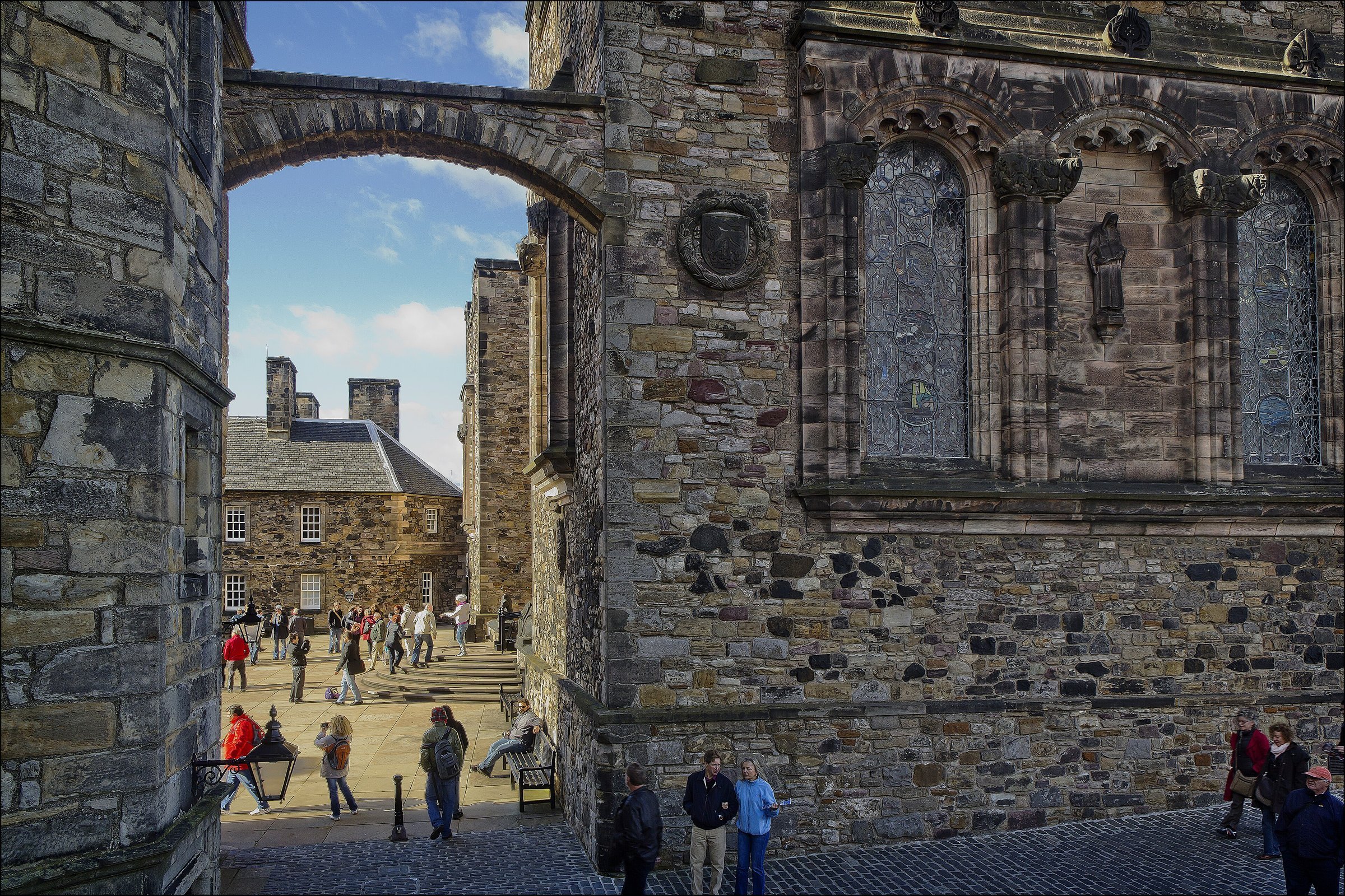 The stone arch leading into Crown Square at Edinburgh Castle, with the Scottish National War Memorial on the right and visitors on the steps