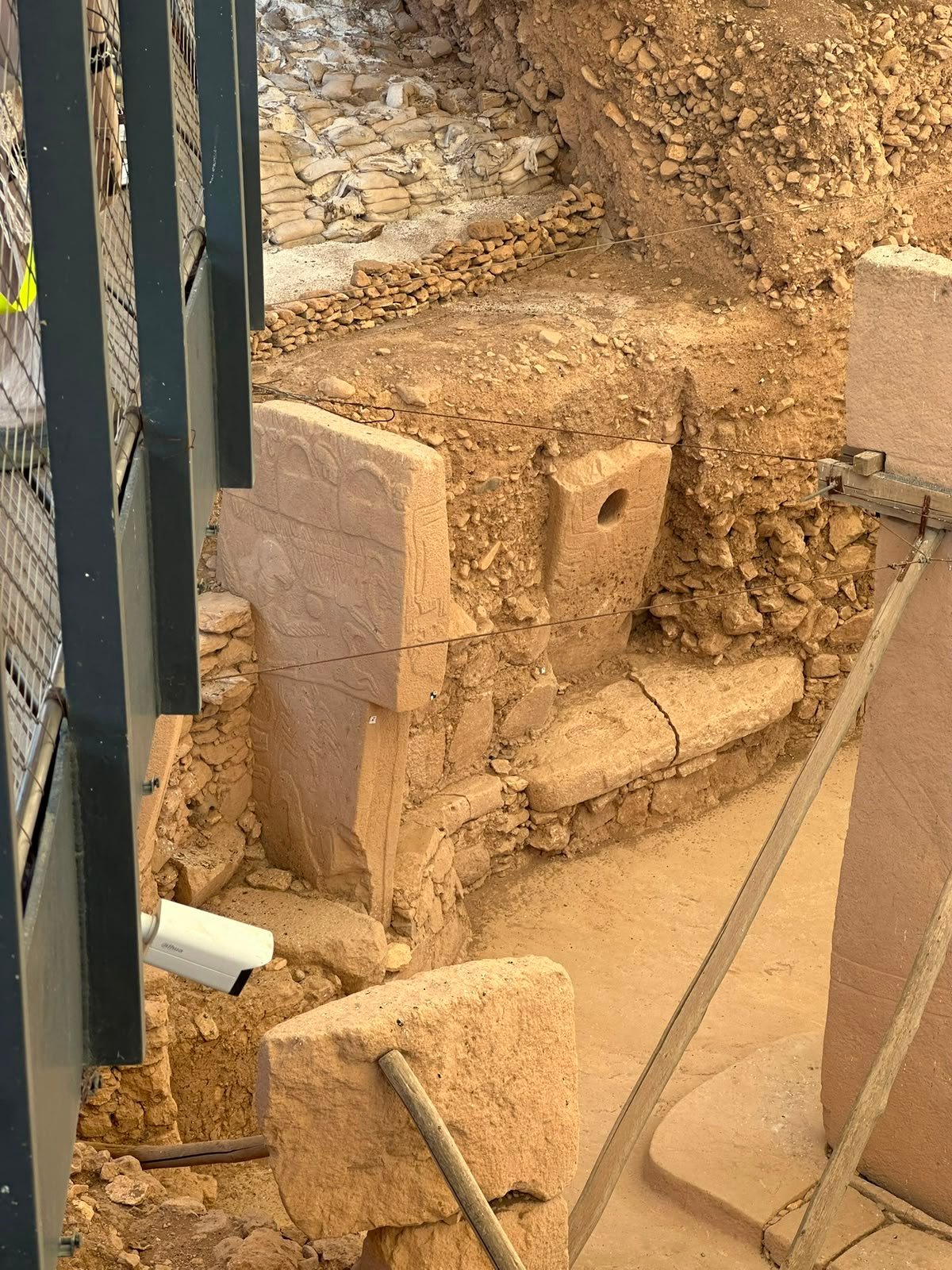 A carved limestone pillar and a porthole stone in a partly excavated enclosure, with sandbags holding the trench wall.