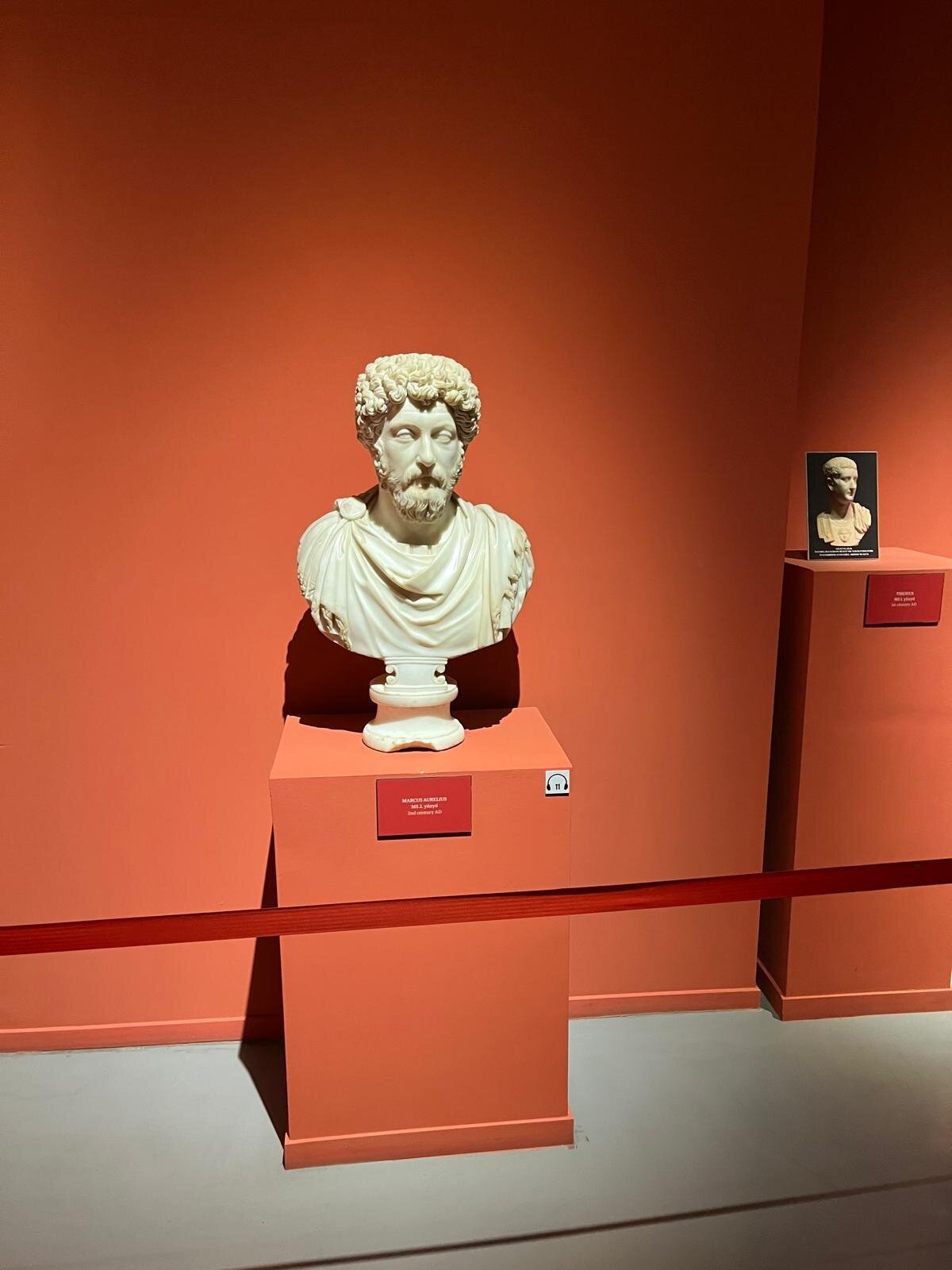 A marble bust of Marcus Aurelius lit on a pedestal in an indoor museum gallery.