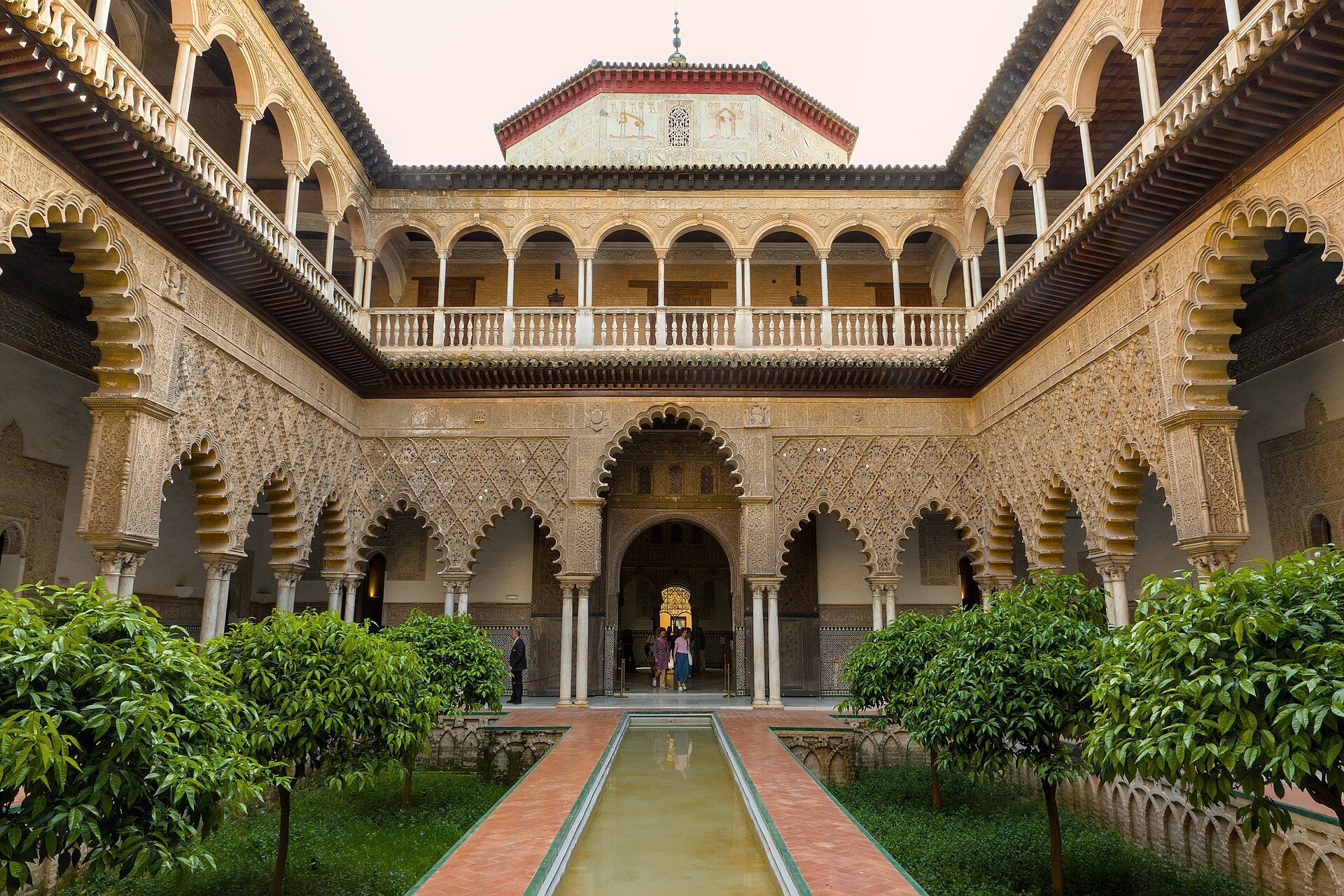 Sevilla Real Alcázar'ındaki Bakireler Avlusu; çukur bahçelerin arasında uzun bir havuz ve oyma kemerli revaklar