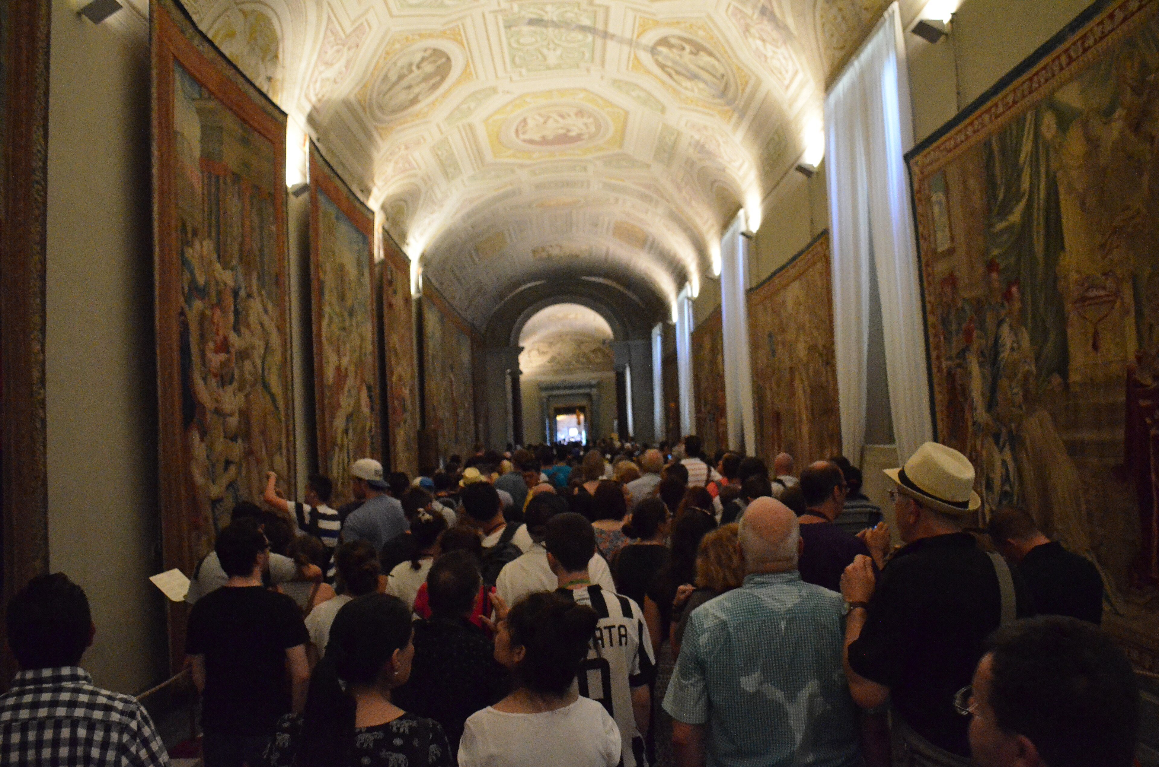 Visitors crowding the Gallery of Tapestries in the Vatican Museums under a painted vaulted ceiling